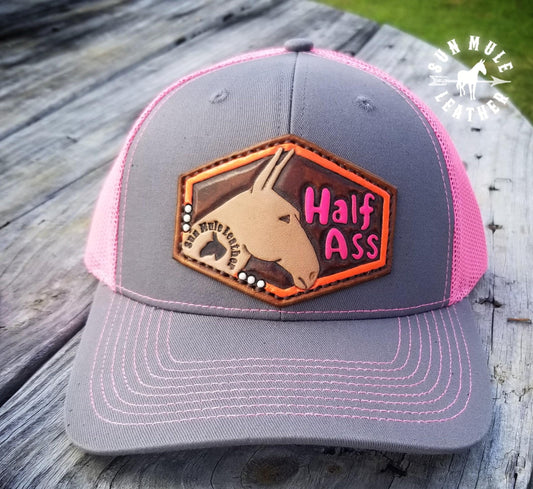 Pink trucker mule hat, leather hand tooled patch depicting a mule and the words "half ass". 