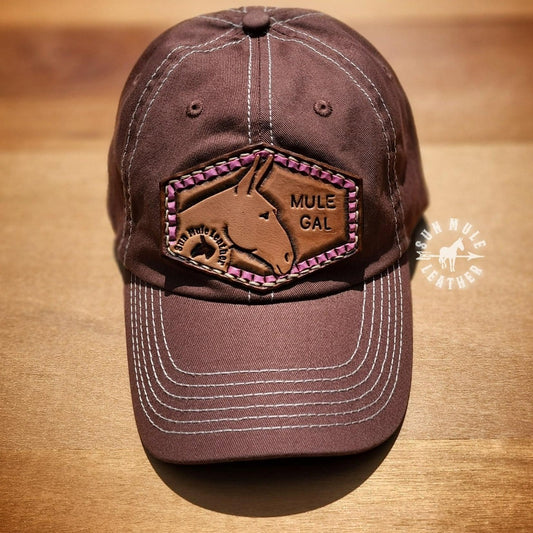 Handtooled leather patch with a mule and pink ribbon border with the stamped words "Mule Gal". 