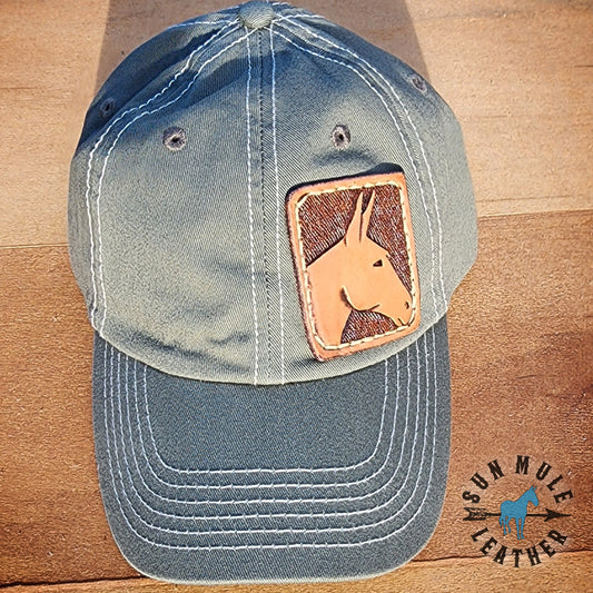 Small rectangular hand tooled mule head leather patch  sewed onto right side front of an Olive colored unstructured hat.